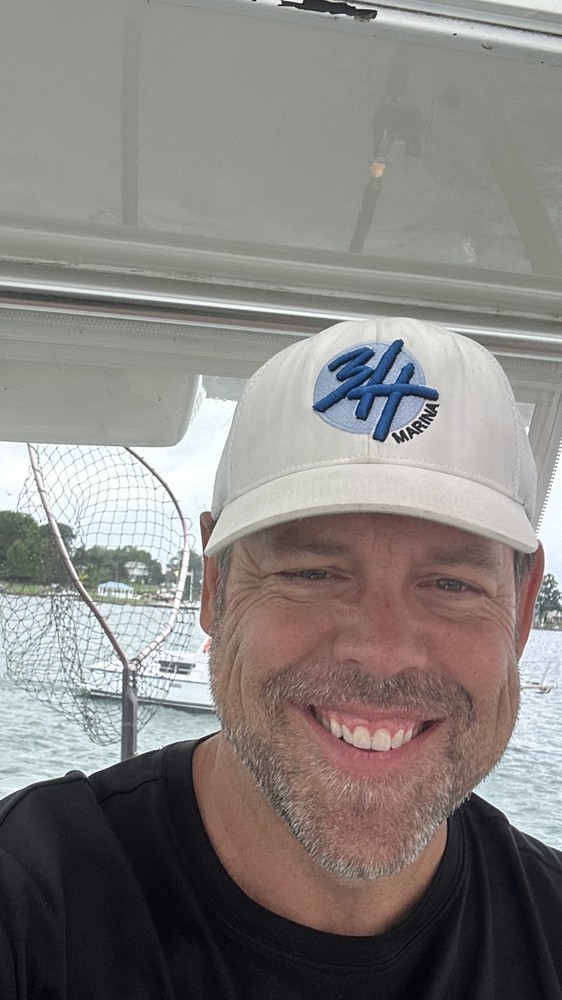 Jeffrey R. Hubbard, founder of 3H Marina, aboard his boat on open water wearing the 3H Marina cap.