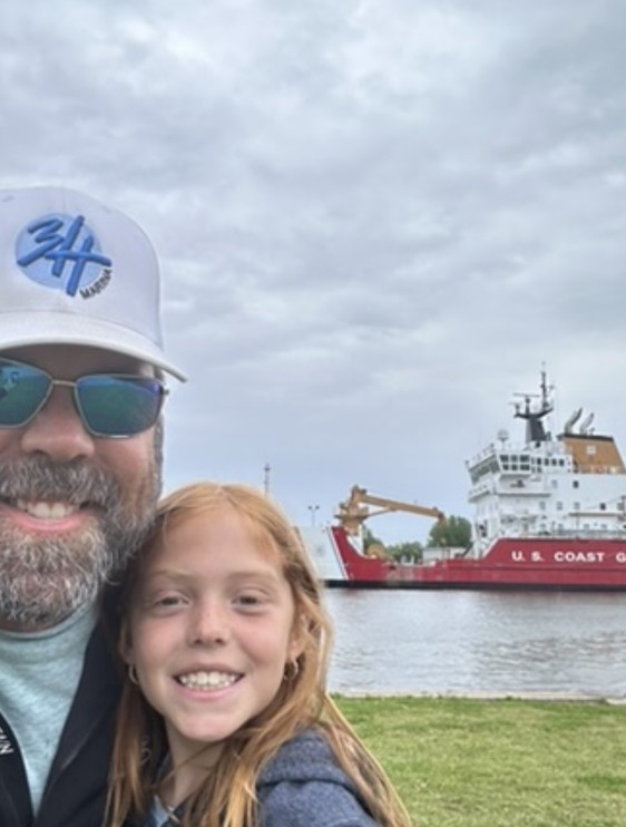 Penelope Grace Hubbard with Jeffrey and a U.S. Coast Guard ice breaker on the water.