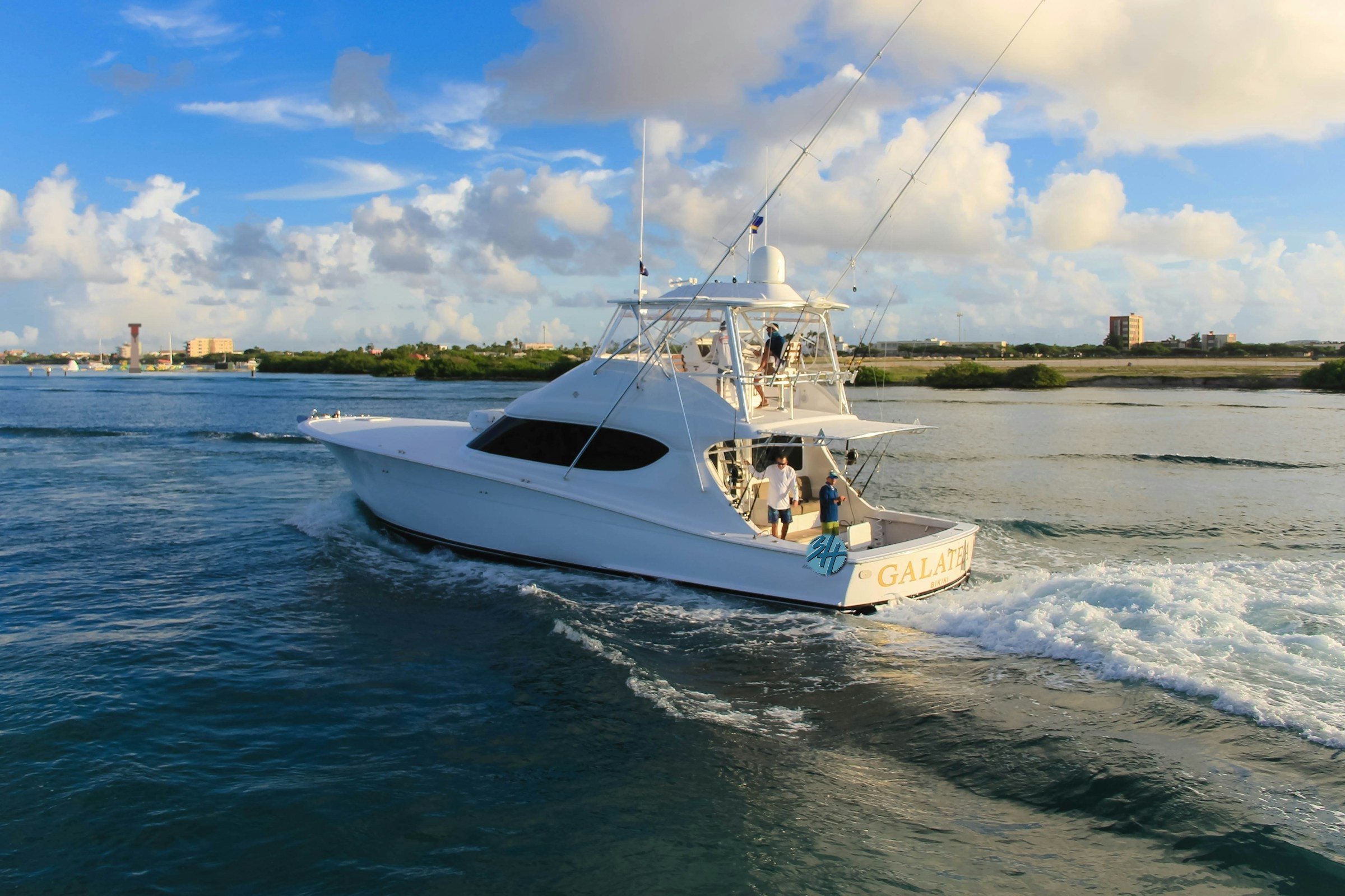 An enclosed flybridge sportfishing yacht with the 3H Marina logo on the stern, cruising on open blue water with a Great Lakes lighthouse on the distant shoreline.